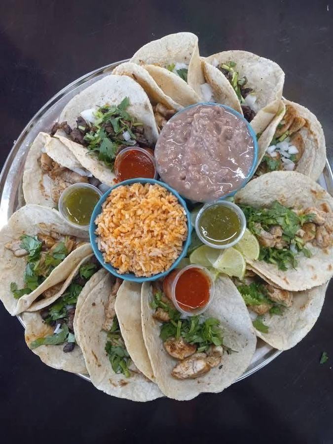A platter of corn tortilla tacos with cilantro and onion, rice, beans, and red and green salsas